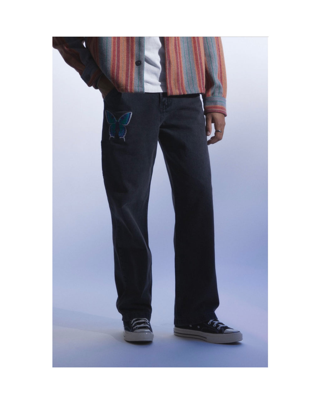 Person wearing black denim pants with a blue butterfly design on a white background