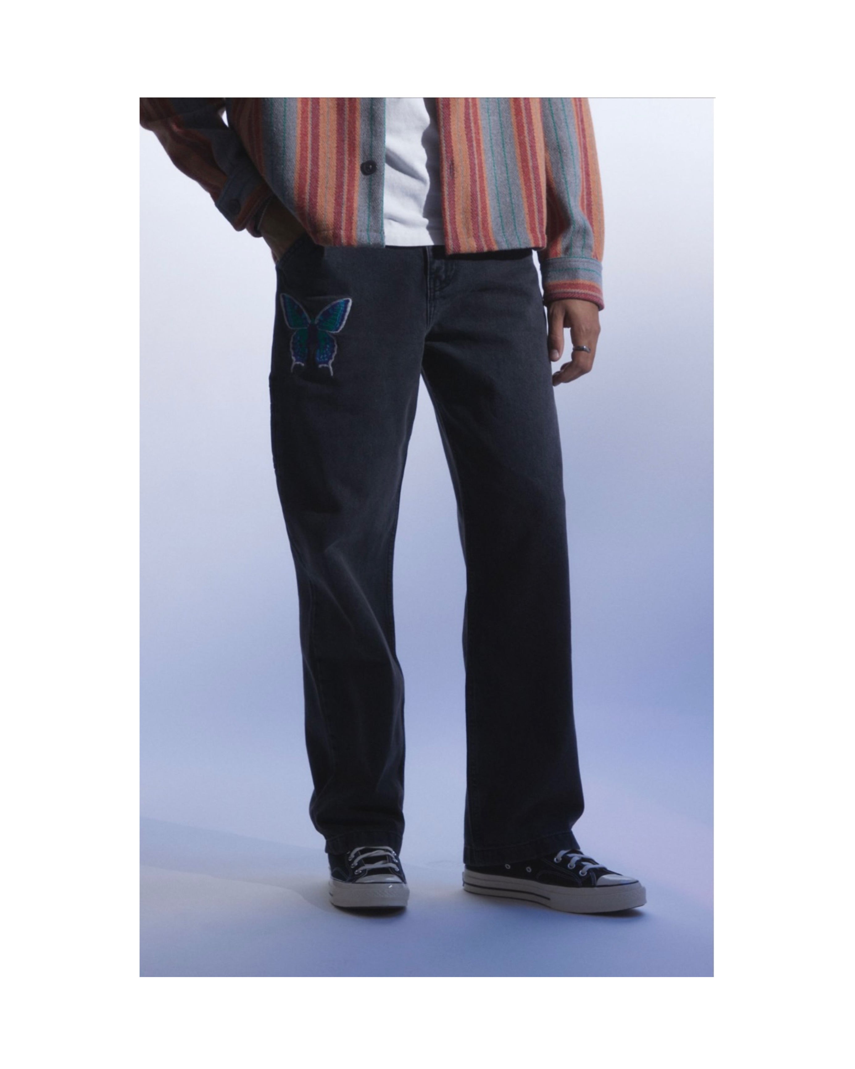 Person wearing black denim pants with a blue butterfly design on a white background