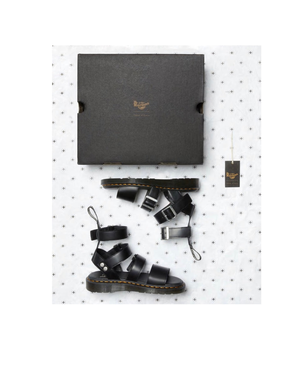 Black leather sandals with straps on a white pegboard with a Dr. Martens box.