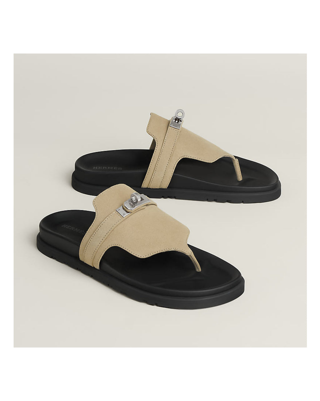 Pair of beige and black sandals with metallic accents on a light beige background