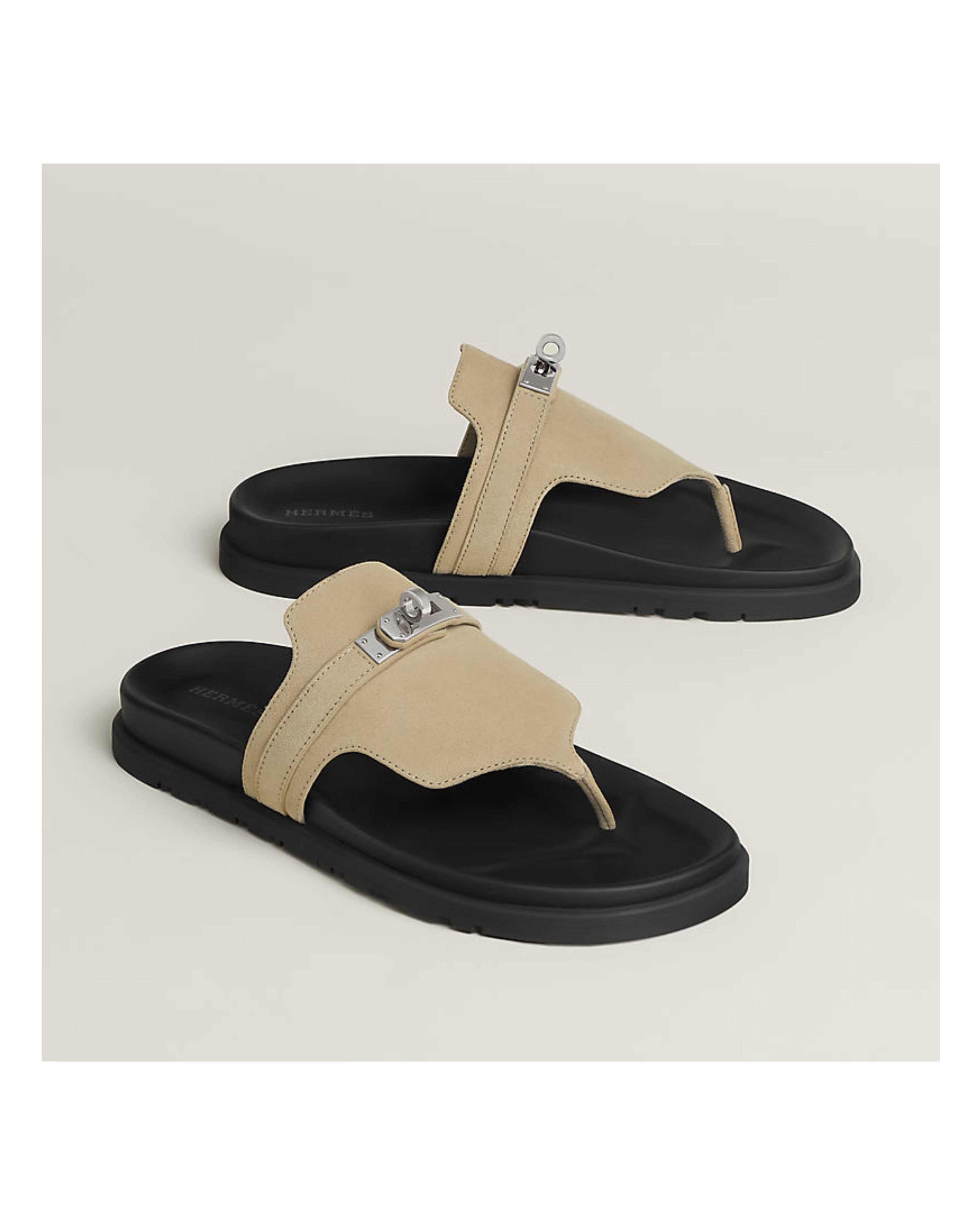 Pair of beige and black sandals with metallic accents on a light beige background