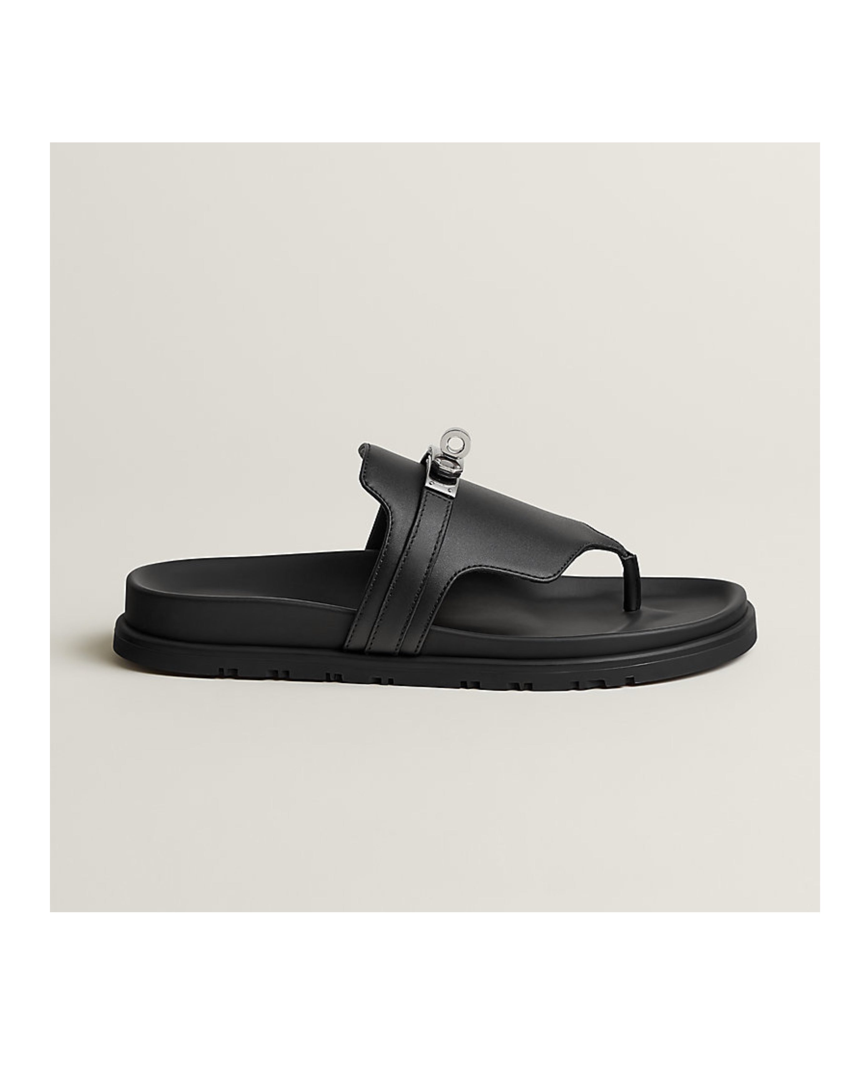 Black sandal with a unique strap design on a light beige background