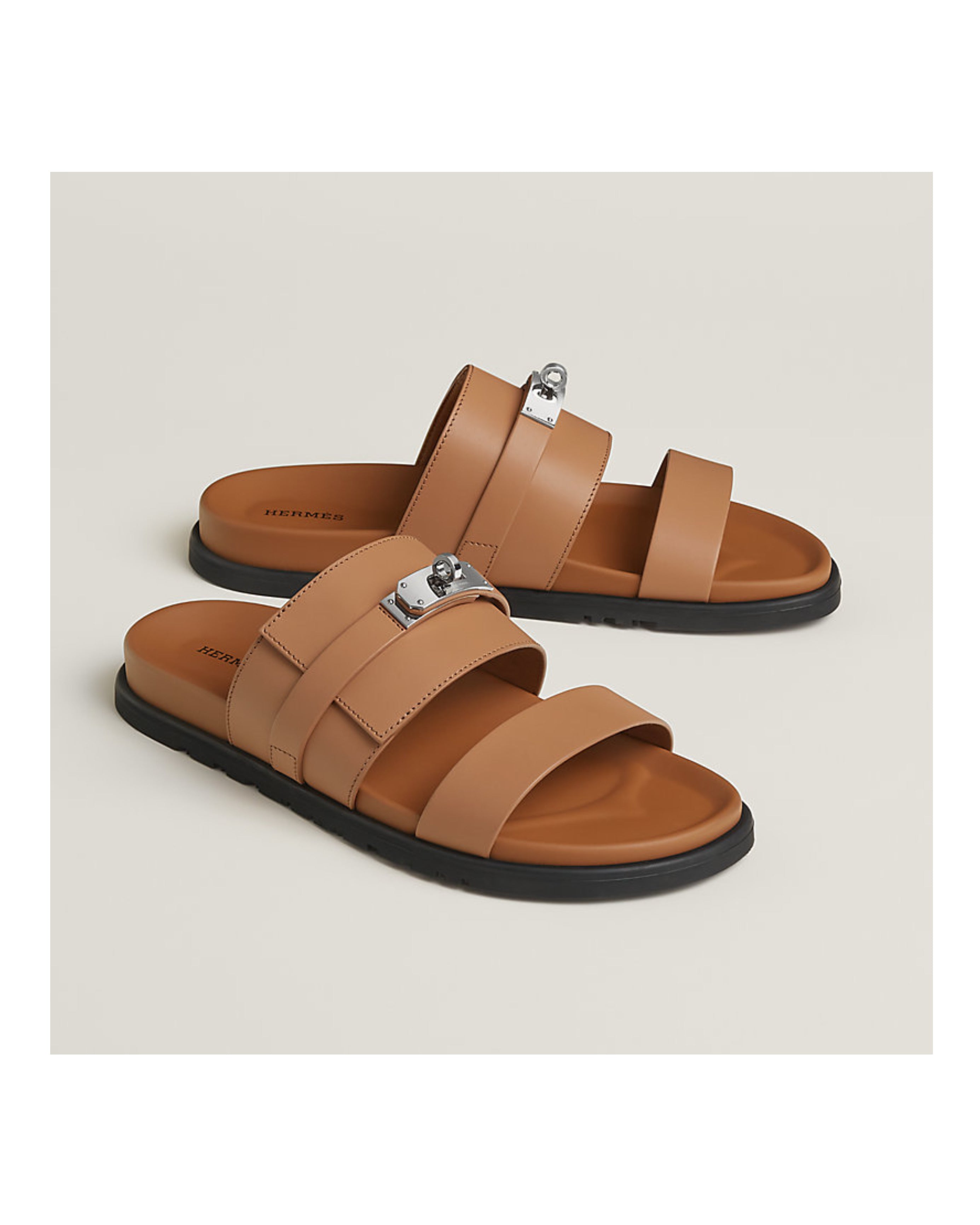 Pair of tan sandals with a silver buckle on a beige background