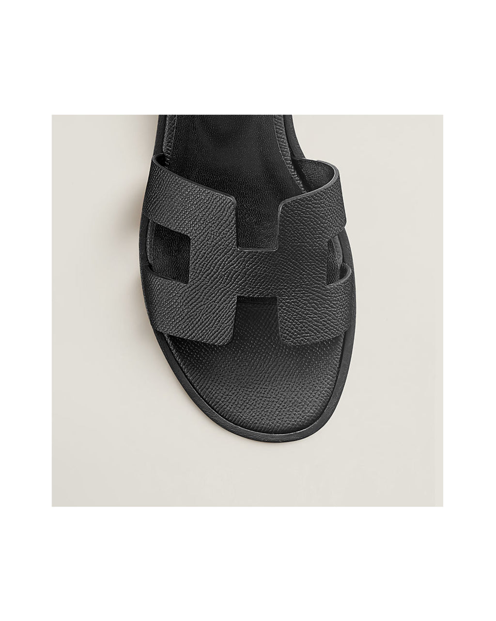 Black sandal with a distinctive strap design on a light beige background