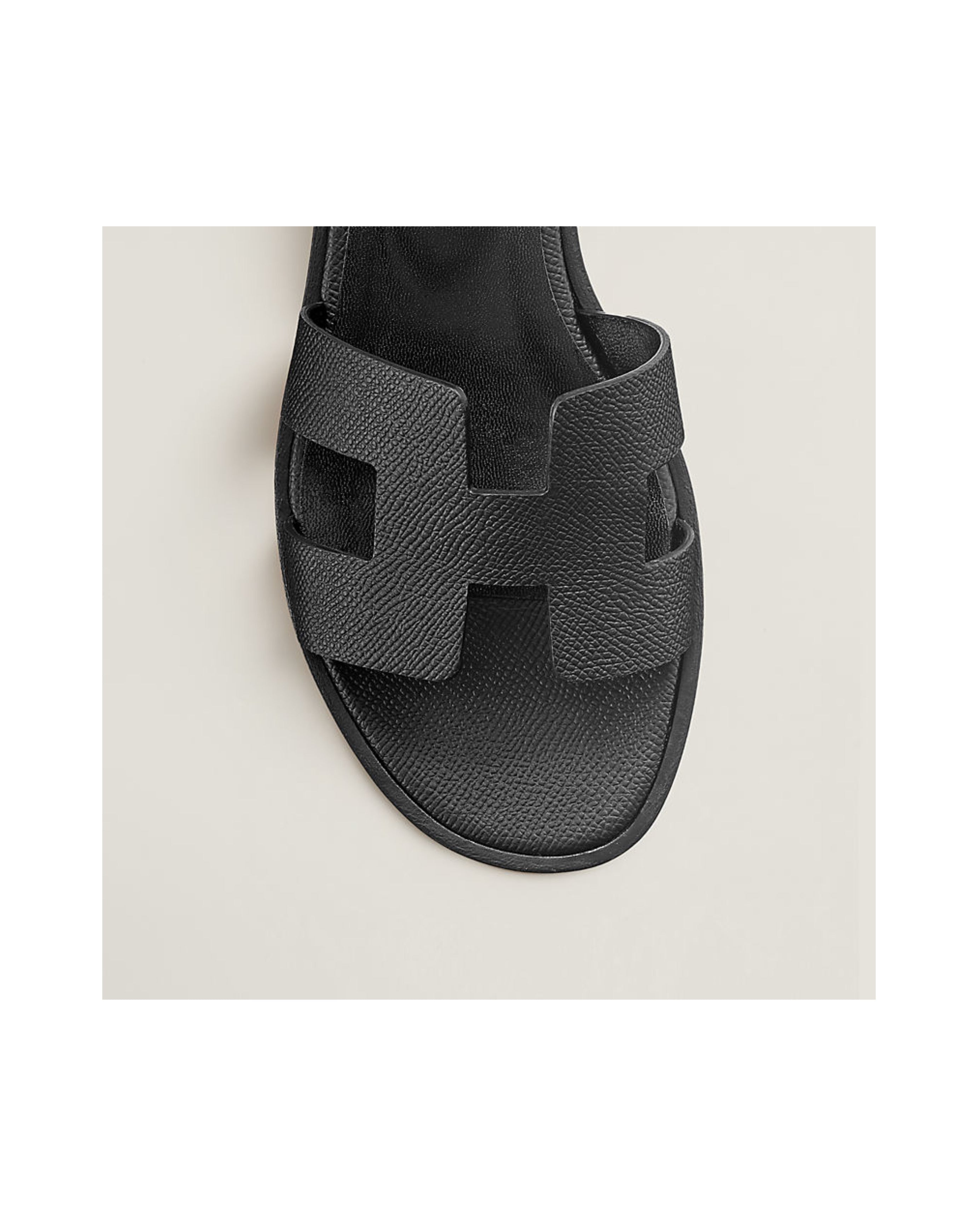 Black sandal with a distinctive strap design on a light beige background