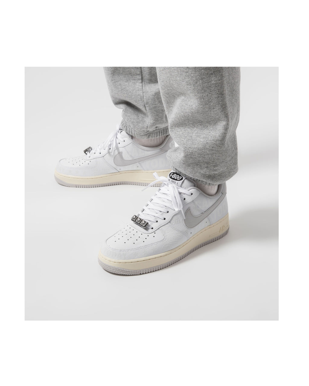 White sneakers with beige soles worn with gray sweatpants on a white background